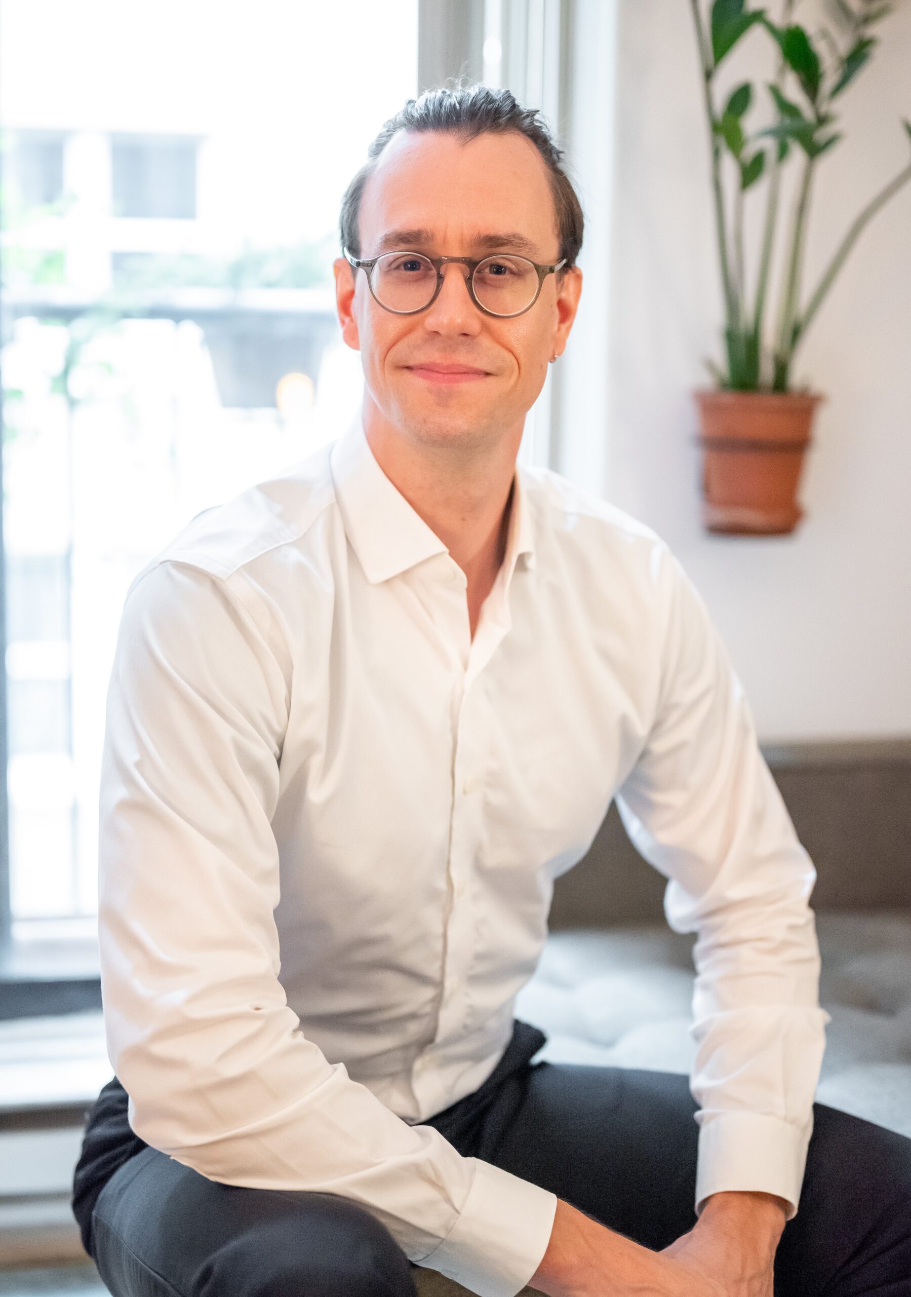 A portrait photo of Alexander Beznes sitting on the couch in his office.